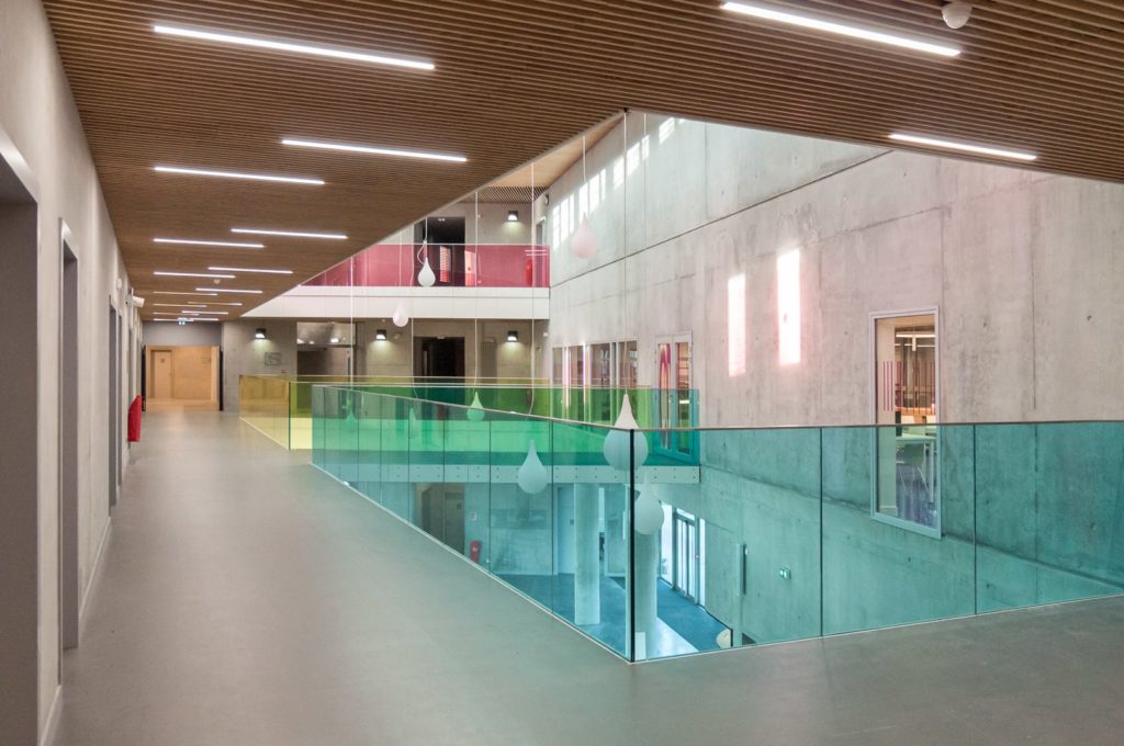 atrium intérieur avec un plafond bois et des gardes corps en verre coloré bleu, jaune et rose
