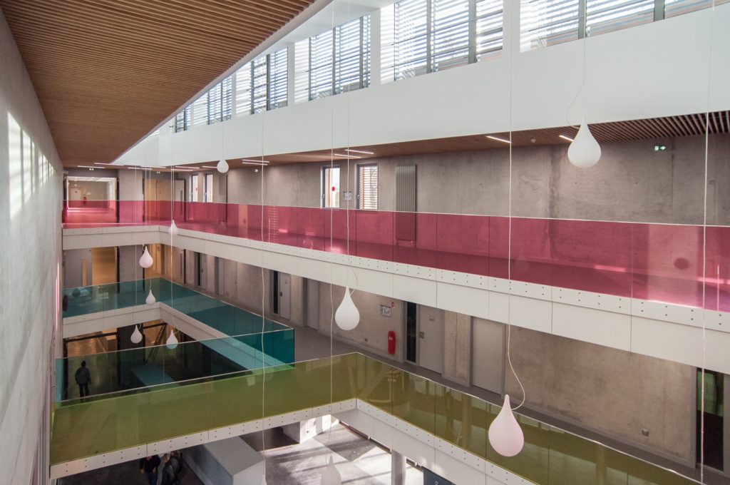 atrium intérieur avec des lustres et des gardes corps en verre coloré bleu, jaune et rose
