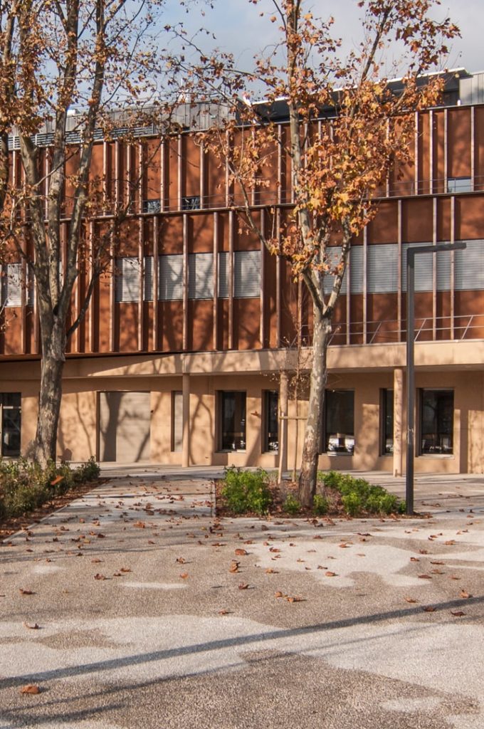 façade en bois et en béton coloré et au premier plan une cour d'école