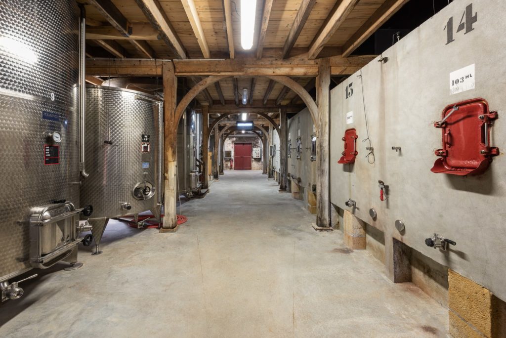 Un chai avec des cuves à vin en inox et en béton ainsi qu'une charpente en bois